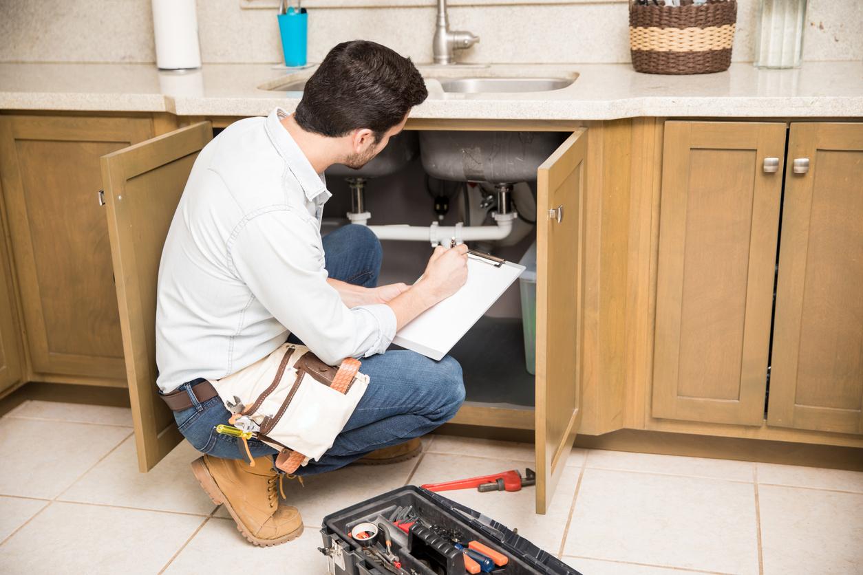 Plumber inspects pipes under sink and takes notes